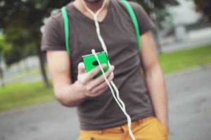 Teenage boy walking with handheld device with earphones attached. Image is just of his torse