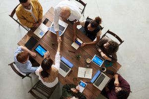 A group og 8 professionals sat at a meeting table with various different devices open infront of them