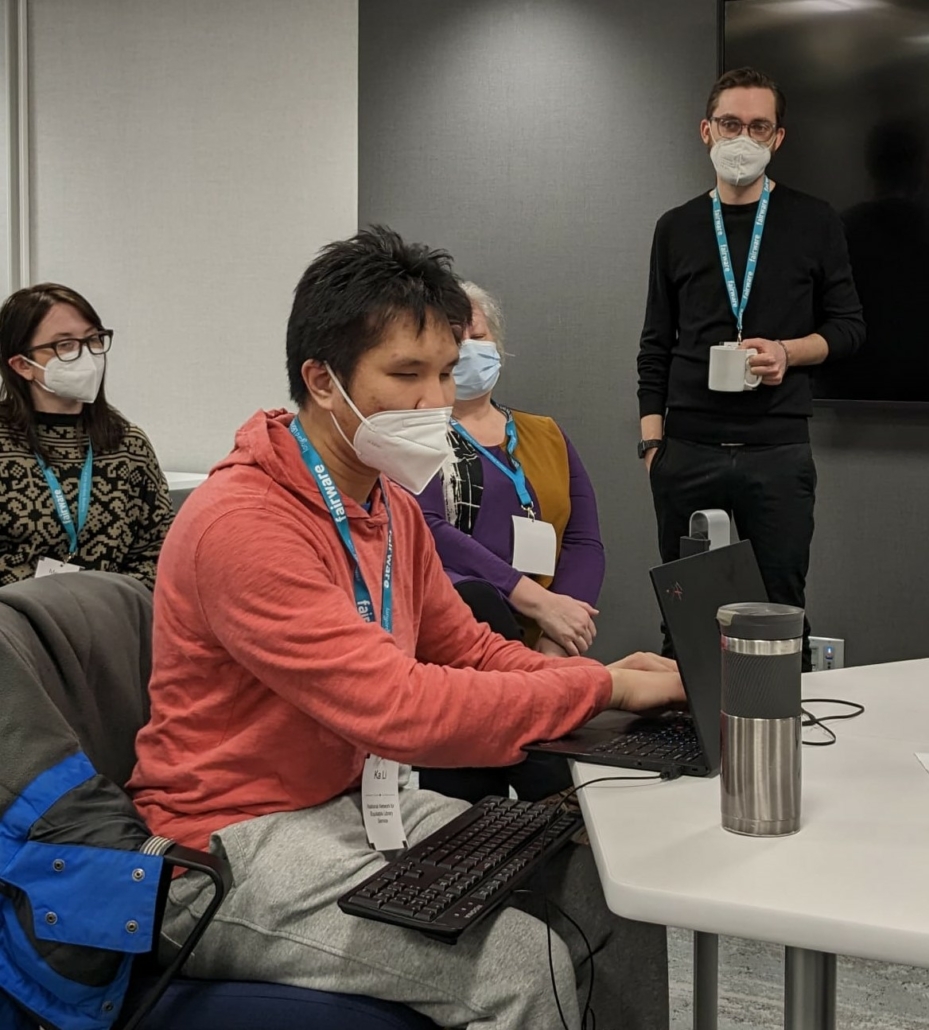 Kai Li sitting at a table reading on his laptop and with a keyboard on his lap