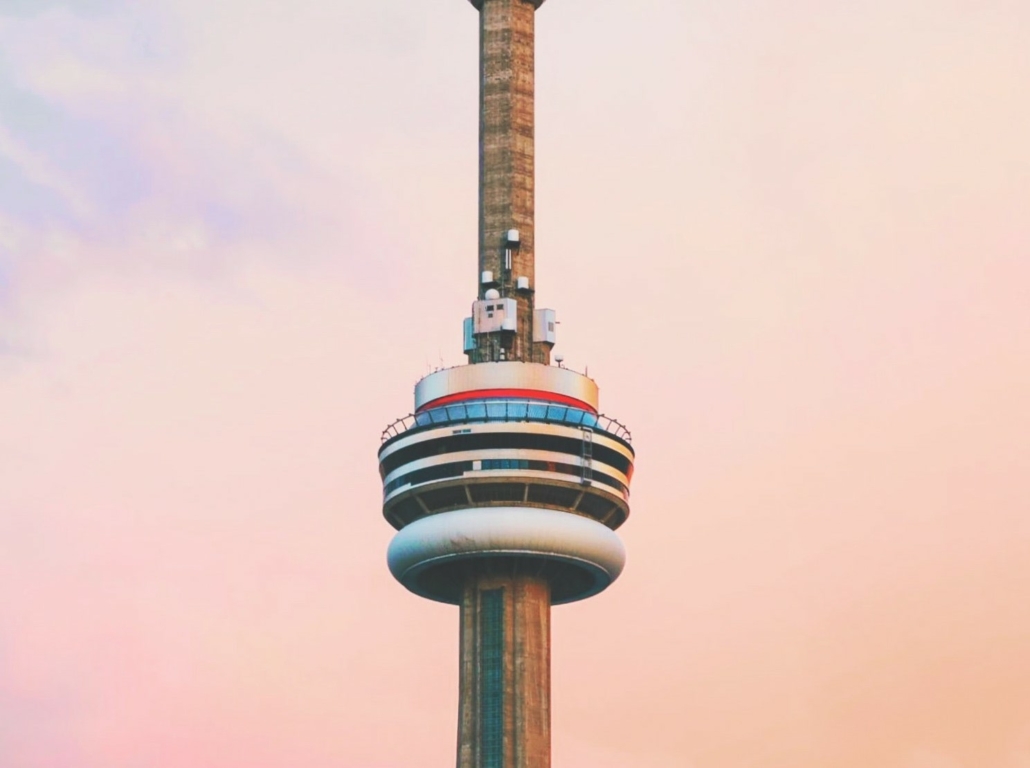 The top section of the CN tower against a pink sky