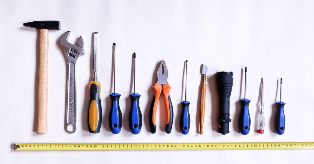 A range of workshop tools laid out in line on a white surface with a tape measure underneath