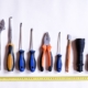 A range of workshop tools laid out in line on a white surface with a tape measure underneath