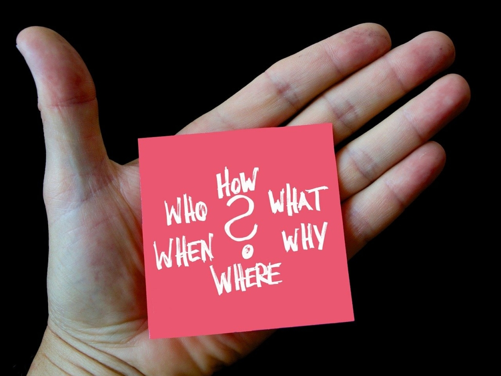 photograph of an open hand with a post note on the palm reading "how, who, what, when, why and where?"