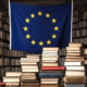 the EU flag amongst a series of full bookcases and a desk piled high with books