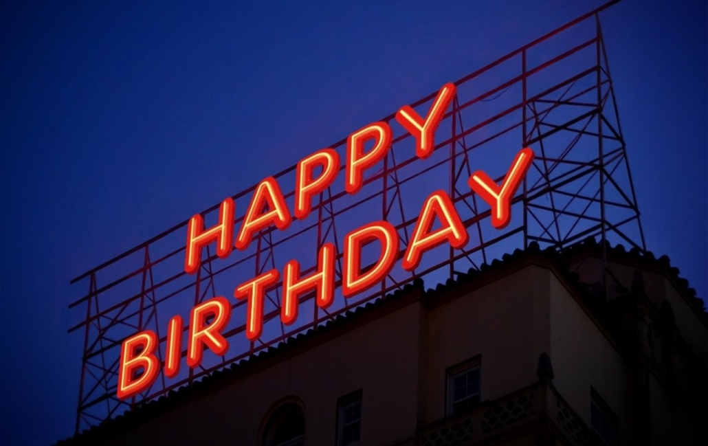 A large neon sign on top of a building at night which reads Happy Birthday