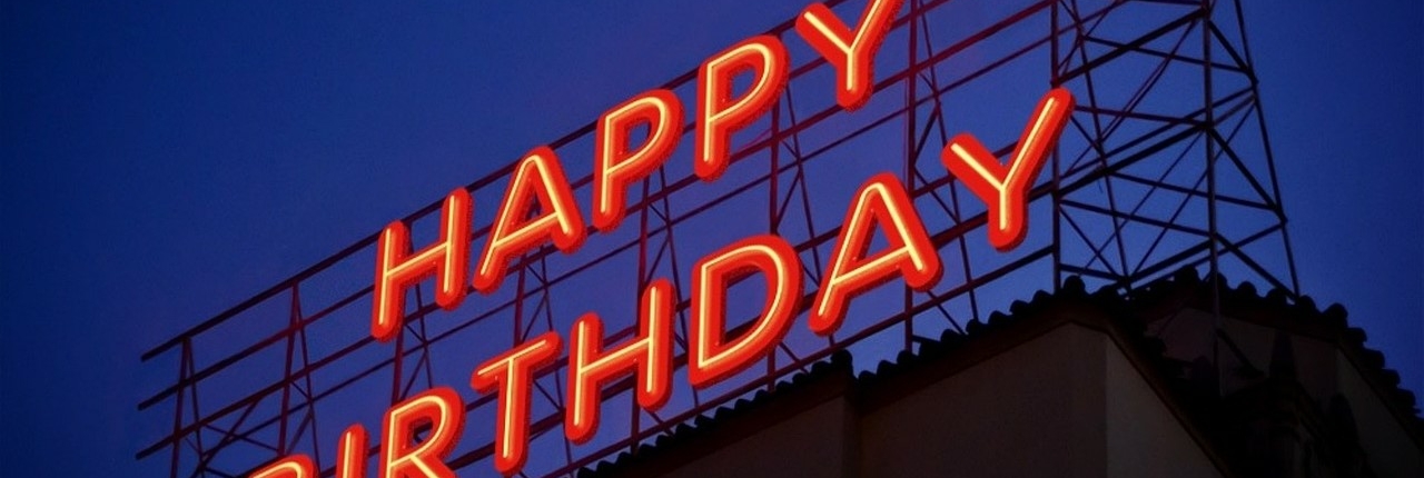 A large neon sign on top of a building at night which reads Happy Birthday