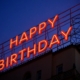 A large neon sign on top of a building at night which reads Happy Birthday